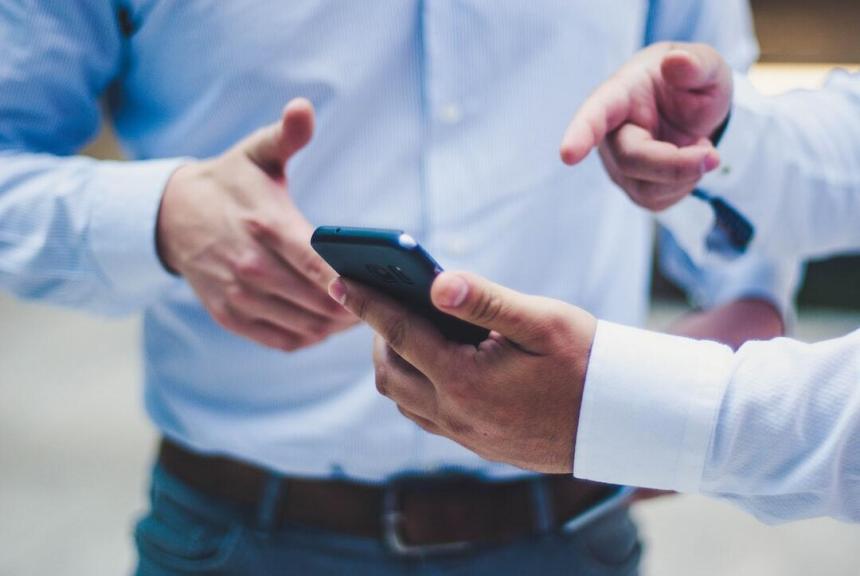 Two men in blue oxford shirts point at a phone screen